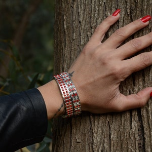May include: A woman's wrist adorned with two silver bracelets featuring rows of red and clear rhinestones. The bracelets are stacked on top of each other.