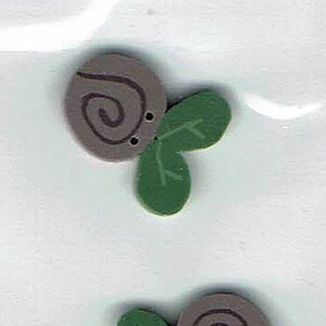 May include: Two brown and green wooden buttons with a swirl design and two holes. The buttons are shaped like a snail with a leaf.