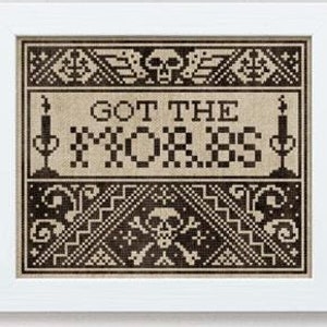 Op de afbeelding: Een ingelijst kruissteekontwerp met de tekst "GOT THE MORBS" in een gotisch lettertype. Het ontwerp bevat schedels, kaarsen en geometrische patronen in zwart en bruin. De woorden "dark crosses" staan bovenaan.