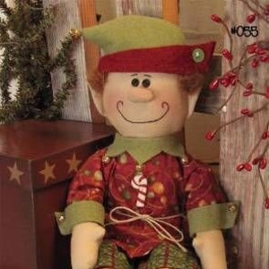 May include: A green and red Christmas elf doll with a candy cane in its hand. The elf is sitting down with its legs crossed and is wearing a green hat with a red band and a red and green patterned shirt. The elf is 8 inches tall.
