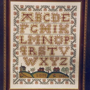 May include: A framed cross-stitch sampler featuring the alphabet in a traditional style. The letters are embroidered in red, yellow, and green thread on a white background. The sampler is surrounded by a decorative border of flowers and leaves.