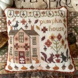 Może przedstawiać: Biała poduszka z haftem krzyżykowym przedstawiającym mały domek, dynie, wiewiórki i napis "pumpkin house".