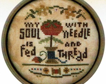 Op de afbeelding: Een borduurwerk met kruissteek in een ovaal frame met de tekst "My soul is fed with a needle and thread". Het ontwerp bevat een rode bloem met groene bladeren en een spoel garen.