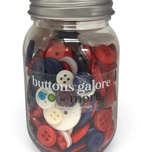 May include: A clear jar filled with red, white, and blue buttons. The jar has a silver lid and the words "buttons galore & more" are printed on the front. A variety of button sizes and styles are visible.