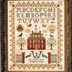 May include: A framed cross-stitch sampler featuring a red brick house with a white door and windows, surrounded by a green border with flowers and birds. The alphabet is stitched in brown and the text reads "The Home Sweet Home of Elizabeth Wray".