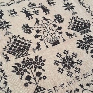 May include: Black and white cross-stitch embroidery pattern on a beige linen fabric. The design features a variety of motifs including birds, flowers, trees, and geometric shapes.