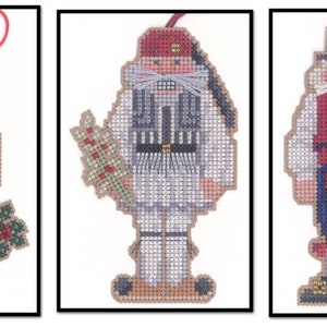 May include: Three Christmas ornaments featuring stylized figures in traditional clothing. The first ornament features a figure wearing a blue and red striped shirt, brown pants, and a red hat. The second ornament features a figure wearing a white shirt, black vest, and a red hat. The third ornament features a figure wearing a red vest, blue pants, and a black hat.