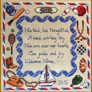May include: Cross-stitch embroidery with a blue and white wavy border. The center features a poem about a kind and hardworking boy. The poem reads: "He's kind, he's thoughtful, A hard-working boy. He's won over our hearts, Our pride and joy. Welcome Home." The year 2015 is stitched in red below the poem. The border is decorated with various sports-themed icons, including a baseball bat, a basketball, a bowling pin, a sailboat, and a hockey stick.