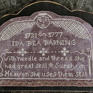 Op de afbeelding: Een zwarte houten plaquette met een wit geborduurd ontwerp. De plaquette toont een grafsteen met de inscriptie "1731 1777 IDA DEA DARNING With needle and thread she had great skill Surely in Meaven she uses them still".