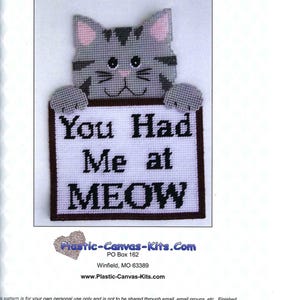 May include: A gray cat with pink ears holding a white sign that says "You Had Me at MEOW". The sign has a brown border. This is a plastic canvas kit.