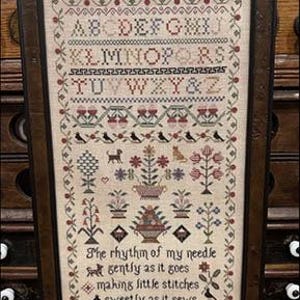 May include: Framed cross-stitch sampler with the text "The Rhythm of My Needle" at the top. The sampler features an alphabet, floral and bird motifs, and the text "The rhythm of my needle gently as it goes making little stitches sweetly as it sews."