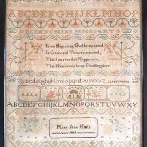 Puede incluir: Un sampler enmarcado con un poema y un alfabeto bordado en hilo de colores. El sampler está fechado en 1813 y firmado "Mary Ann Kittle".