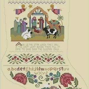 May include: A beige Christmas stocking with cross-stitch embroidery. The design features a nativity scene, angels, floral patterns, and the alphabet. The word "NAME" is stitched at the top, and a Bible verse is included.