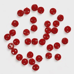 Peut inclure: Plusieurs petits boutons ronds rouges, chacun percé de deux trous, sont disposés sur un fond blanc. Les boutons présentent une surface légèrement texturée et sont espacés de manière uniforme. Idéal pour la couture et les travaux manuels.