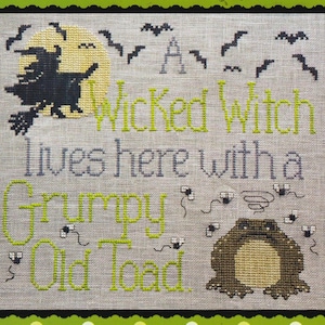 May include: Cross-stitch design with a Halloween theme. The design features a witch on a broom in front of a yellow moon, bats, and the text "A Wicked Witch lives here with a Grumpy Old Toad."