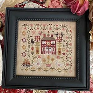 May include: Framed cross-stitch artwork featuring a red house with a floral border. The artwork includes various floral and heart motifs in shades of red, pink, and beige, set against a neutral background. The frame is black.