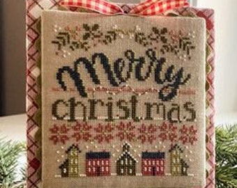 Pode incluir: Um bordado de ponto cruz com um fundo xadrez vermelho e branco e um tecido de linho bege. O bordado apresenta uma cena de inverno com casas, flocos de neve e o texto "Merry Christmas".
