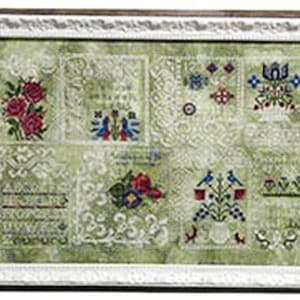May include: A framed cross-stitch sampler with a green background and white embroidery. The sampler features various floral and geometric designs, including a bouquet of red roses, a vase of blue flowers, and a bird motif.