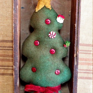 May include: A plush green fabric Christmas tree ornament featuring a gold fabric star topper, a red velvet ribbon bow at the base, and various decorative embellishments including red buttons, a small Santa face, and a peppermint candy accent.