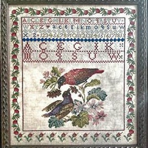 Op de afbeelding: Ingelijste kruissteek sampler met twee vogels op een bloemrijke tak. De sampler bevat een alfabet, cijfers en decoratieve randen met rode bessen en groene bladeren. De lijst is van donker, sierlijk hout.