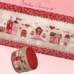 May include: A cross-stitch sampler featuring a row of red and white houses with a heart and the word "LOVE" on the front of one house. The sampler is framed with a red and white border and has a red and white fabric backing.