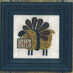 May include: Cross-stitch artwork in a black frame. The image features a stylized sheep with a gift box body and a sign that reads "SALE". The sheep is primarily tan and brown, with black accents.