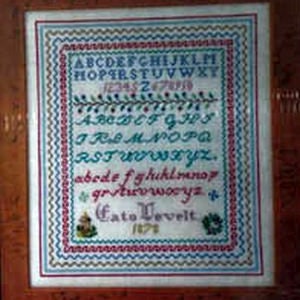 Könnte beinhalten: Ein gerahmter Stich mit weißem Hintergrund und bunter Stickerei. Der Stich zeigt das Alphabet in Groß- und Kleinbuchstaben, sowie Zahlen und ein Blumenmuster. Der Text "Cato Vevelt 1474" ist in der Mitte unten gestickt.