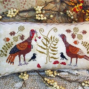 May include: Cream-colored rectangular pillow with a cross-stitch design featuring two turkeys, black birds, and foliage. The turkeys are brown, orange, and red, with the birds in black. The design includes leaves, berries, and mushrooms.