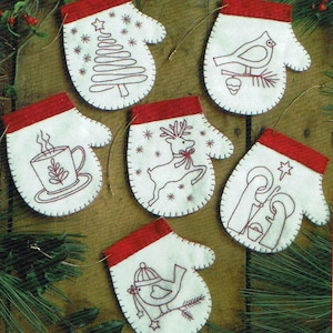 Puede incluir: Seis adornos de fieltro blanco en forma de manopla con puños de fieltro rojo. Cada manopla presenta un diseño bordado diferente: un árbol de Navidad, un cardenal, un reno, una escena de la Natividad, un pájaro con un sombrero y una taza de chocolate caliente.