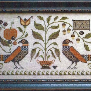Könnte beinhalten: Eine gerahmte Kreuzstich-Stickerei mit einer stilisierten Herbstszene mit zwei Vögeln, einem Kürbis, einem Baum und dem Jahr 1683. Die Stickerei ist in Braun-, Orange-, Grün- und Blautönen gehalten.