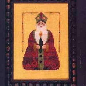 May include: A cross-stitch pattern featuring a stylized Santa Claus figure in red and green clothing, holding a candle. The background is a yellow fabric with a brown frame.