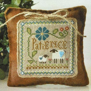 May include: A brown fabric pillow with a cross-stitch design featuring a blue flower, green leaves, two white sheep, and the text "Patience".