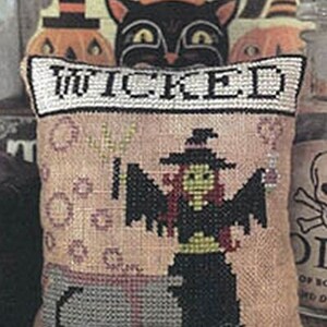 May include: A beige pillow with the word "WICKED" embroidered in black. The pillow features a cross-stitch design of a witch with a cauldron and a black cat.