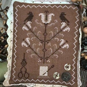 May include: A brown and white cross-stitch cushion featuring a floral design and two birds. The cushion is trimmed with white lace and has three buttons.