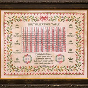 May include: A framed cross-stitch sampler with a red, white, and blue color scheme. The sampler features a multiplication table with a floral border and a quote about kindness. The quote reads: "Multiply kindness, Divide your worry, Subtract sorrow, But most importantly, Add much happiness."