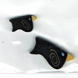 May include: Two black wooden buttons shaped like birds with yellow beaks and blue eyes. Each button has a brown swirl design.