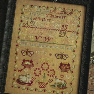 May include: A framed cross-stitch sampler with a brown wooden frame. The sampler features a colorful alphabet, a butterfly, and a floral design. The text "Clarissa Beaumont 1875" is at the bottom of the sampler.