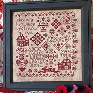 Può includere: Sampler a punto croce incorniciato in una cornice nera. Il sampler presenta una varietà di motivi ricamati in rosso, tra cui case, cuori, fiori, un coniglio e lettere. Lo sfondo è di colore beige chiaro.