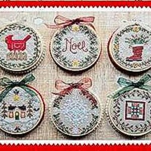 May include: Six embroidered Christmas ornaments in wooden hoops, each with a unique design. The ornaments feature festive motifs like a bird, the word "Noel", a boot, a house, a Christmas tree, and a quilt block. Each ornament is adorned with a ribbon.