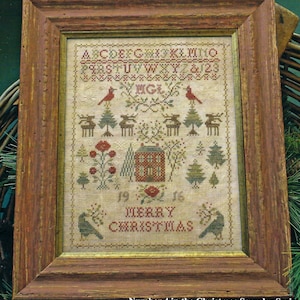 May include: A framed cross-stitch sampler with a red and green color scheme. The sampler features a house, trees, birds, and the text "Merry Christmas".