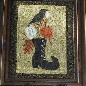 May include: A framed needlepoint design featuring a black crow perched on a branch with white and orange pumpkins in a black boot. The design is set against a beige background with brown and green accents.