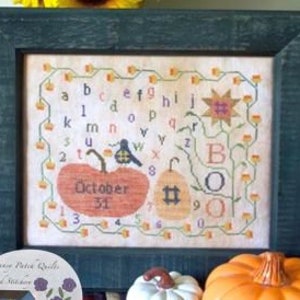 May include: Cross-stitch pattern with an alphabet, pumpkins, and the text "October 31". The design features a black bird, a yellow flower, and a brown vine.