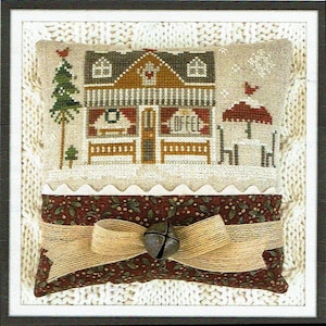 May include: A cross-stitch design of a wintery house with a red roof, a porch, and a sign that says "Coffee". The house is surrounded by snow and a small tree. The design is framed in a white frame with a brown border. A small pillow with a red and green pattern is in the bottom of the frame, with a brown ribbon tied around it and a bell hanging from the bow.