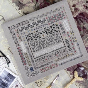 May include: A grey linen fabric with a cross-stitch design featuring a variety of patterns and a quote that reads "Back on its sturdy linses the jate of memory swings 212 my hair jocs into the garden to satser my cxerisex things".