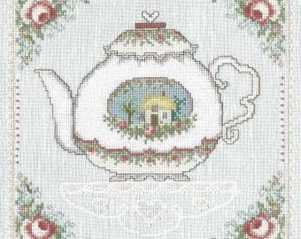 Op de afbeelding: Witte theepot met een bloemenmotief en een klein huisje in het midden. De theepot staat op een wit kantonderzetter en is omringd door een bloemmotief.