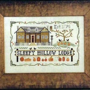 May include: Cross stitch pattern of a house with a sign that reads "Sleepy Hollow Lodge" and the text "Est 1790". The house is brown with white trim and has a white picket fence. There are pumpkins and a tree with birds in front of the house.