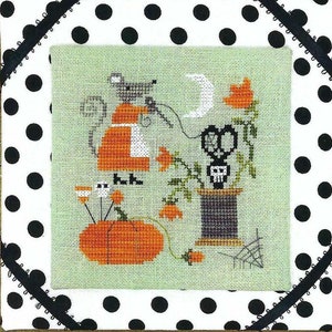 May include: A cross-stitch pattern featuring a black cat, a pumpkin, and a spool of thread with a skull-shaped pair of scissors. The design is set against a green background with a white polka dot border.