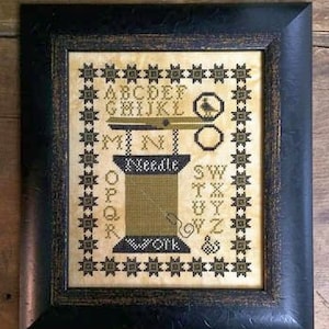 May include: A framed cross-stitch sampler with a black frame and a cream background. The sampler features a needle and thread with the words "Needle Work" and the alphabet in a vintage font.