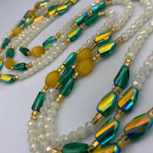May include: A layered necklace with iridescent green and yellow beads, combined with white, faceted beads. The necklace has gold-coloured accents and a delicate design. The beads are arranged in a flowing pattern, creating an elegant look.