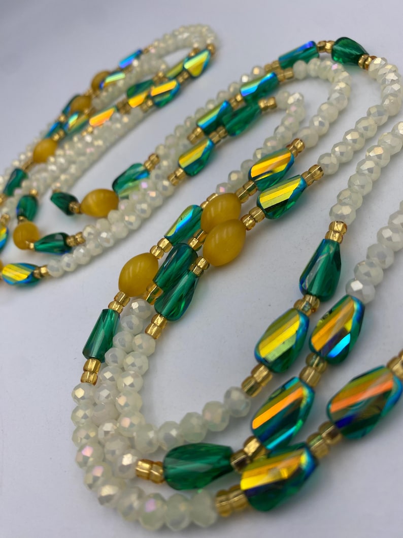 May include: A layered necklace with iridescent green and yellow beads, combined with white, faceted beads. The necklace has gold-coloured accents and a delicate design. The beads are arranged in a flowing pattern, creating an elegant look.